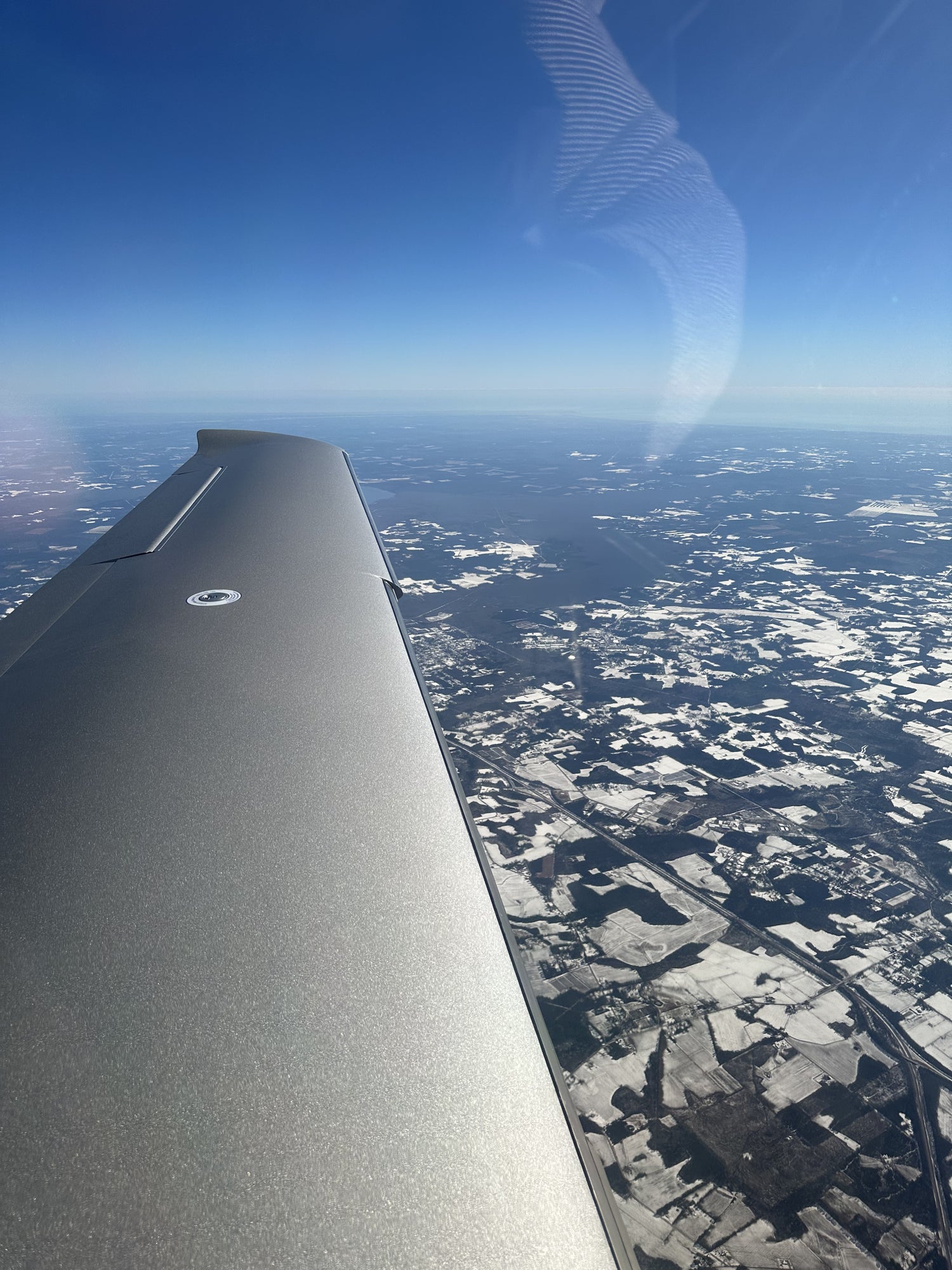 Airplane wing over a landscape with clouds and blue sky

