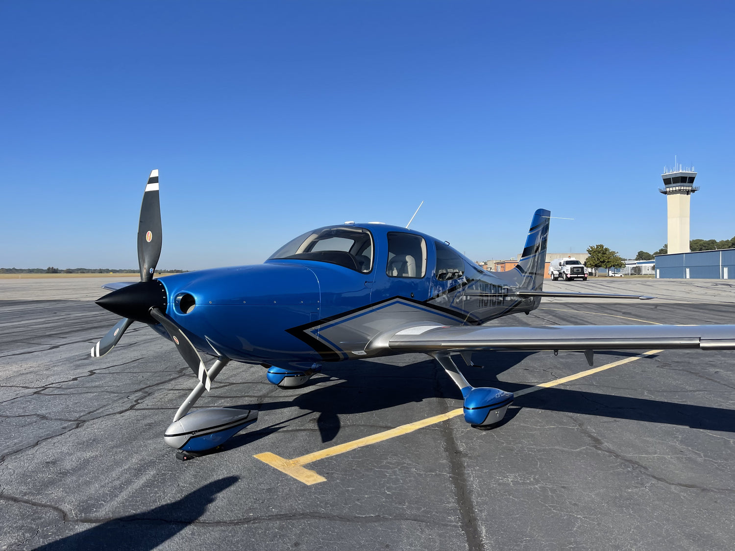 Blue airplane on a runway with control tower in the background

